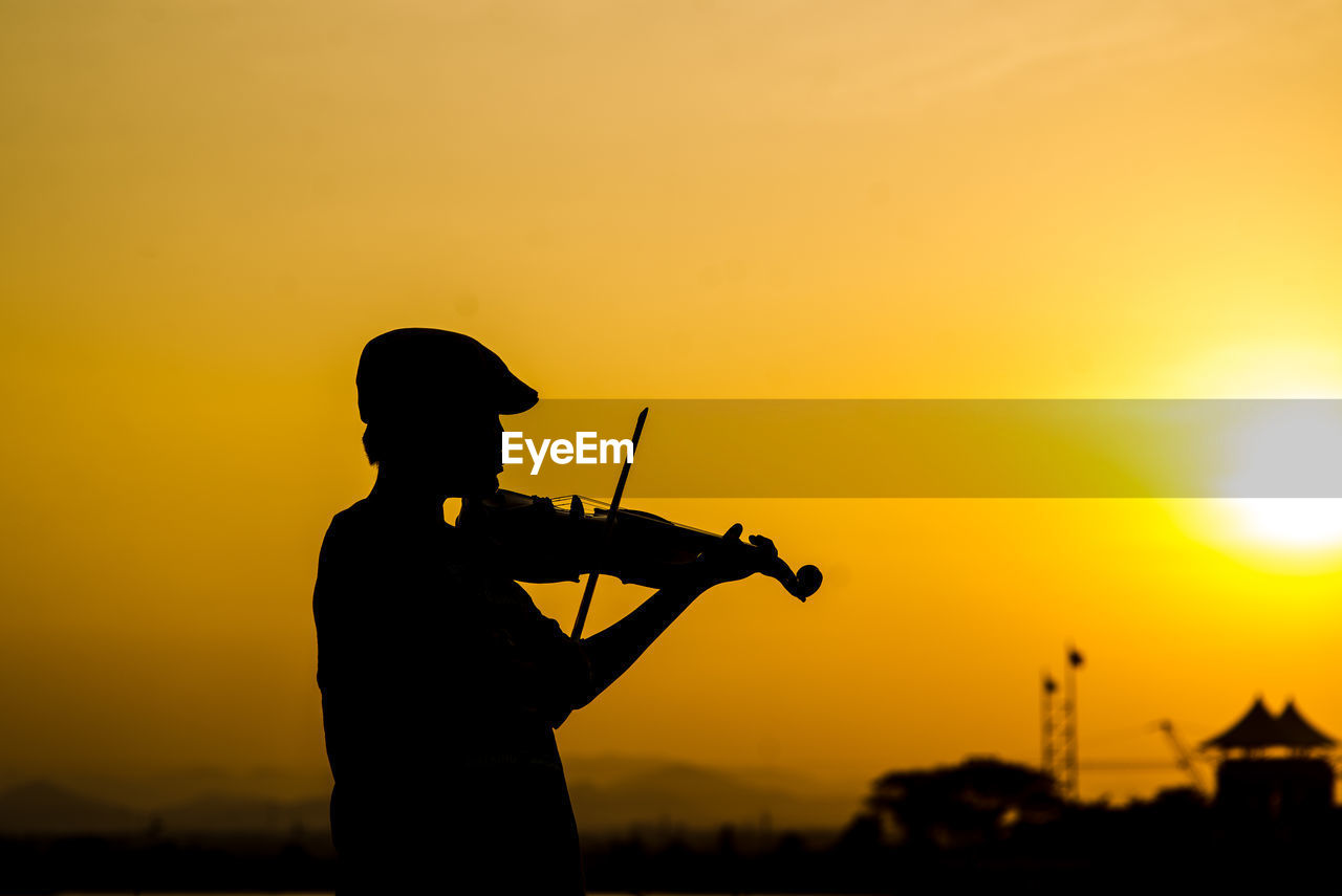 Silhouette boy playing violin against sky during sunset