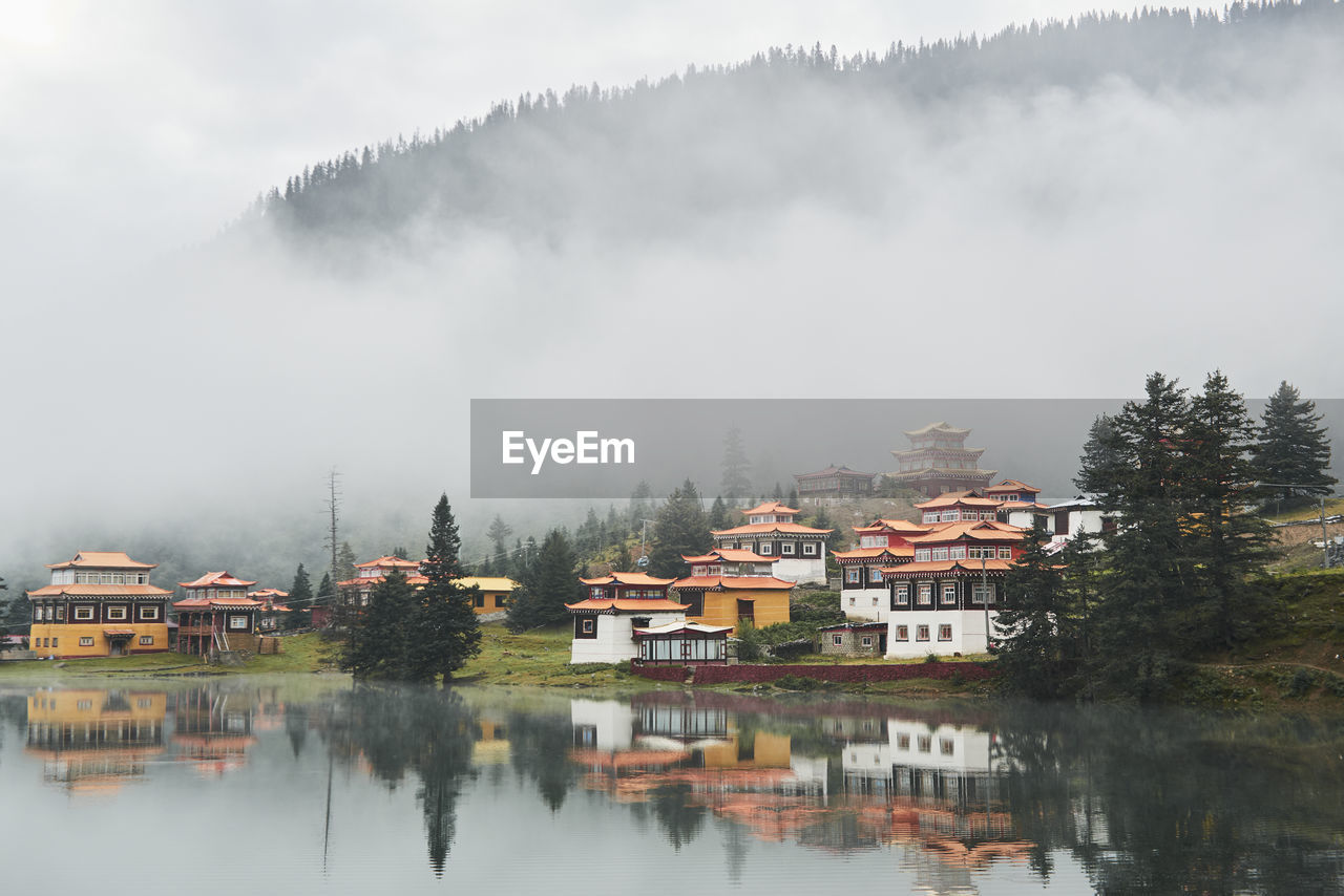 Scenery view of old buildings of tibetan buddhist temples located on shore of tranquil reflecting lake in highland covered with clouds