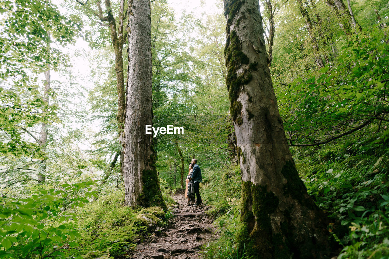 REAR VIEW OF WOMAN WALKING ON TRAIL IN FOREST