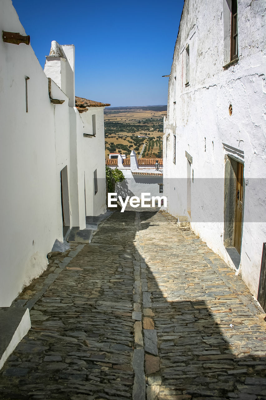 Footpath amidst buildings in town against clear blue sky