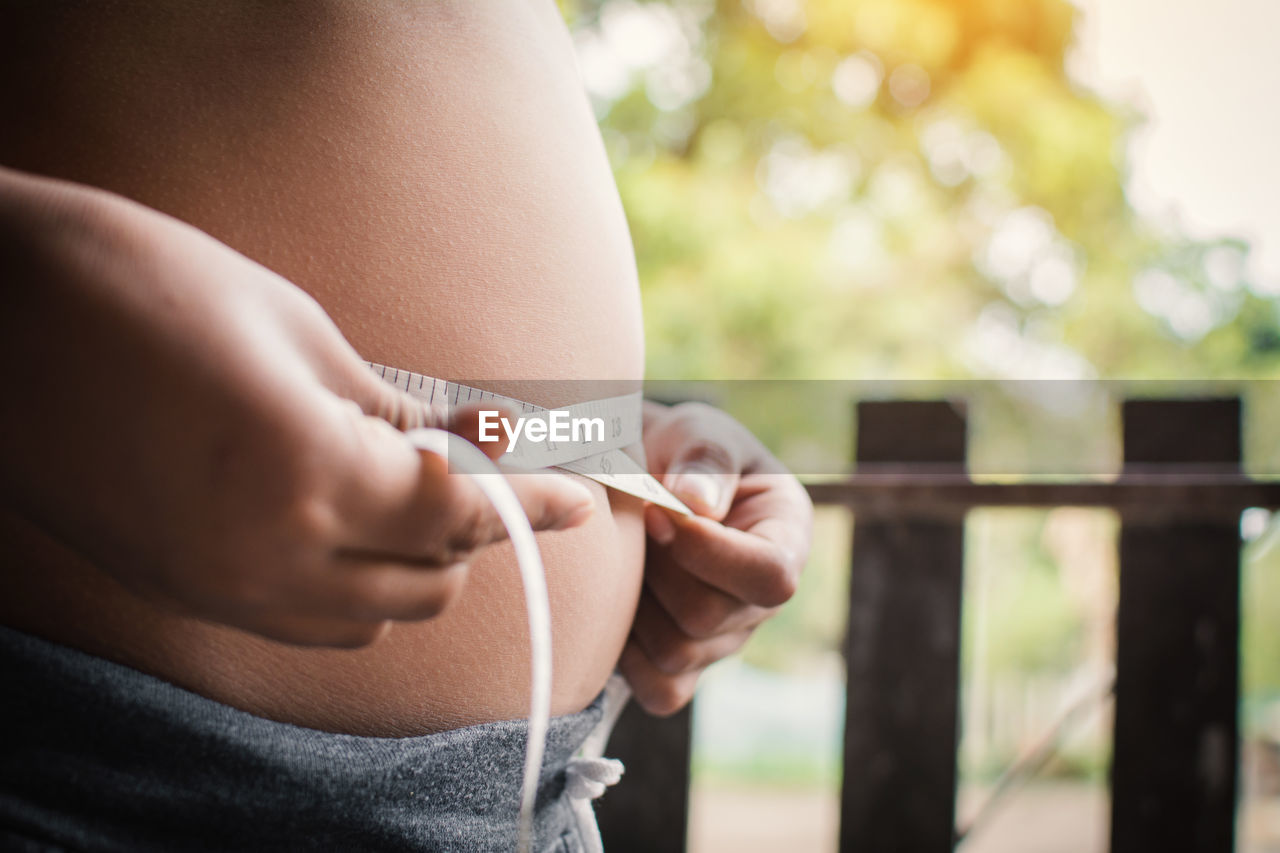 Midsection of pregnant woman measuring abdomen with tape measure