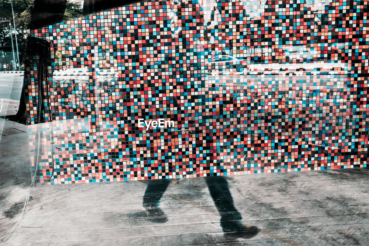 Double exposure of mosaic wall and low section of man walking on street