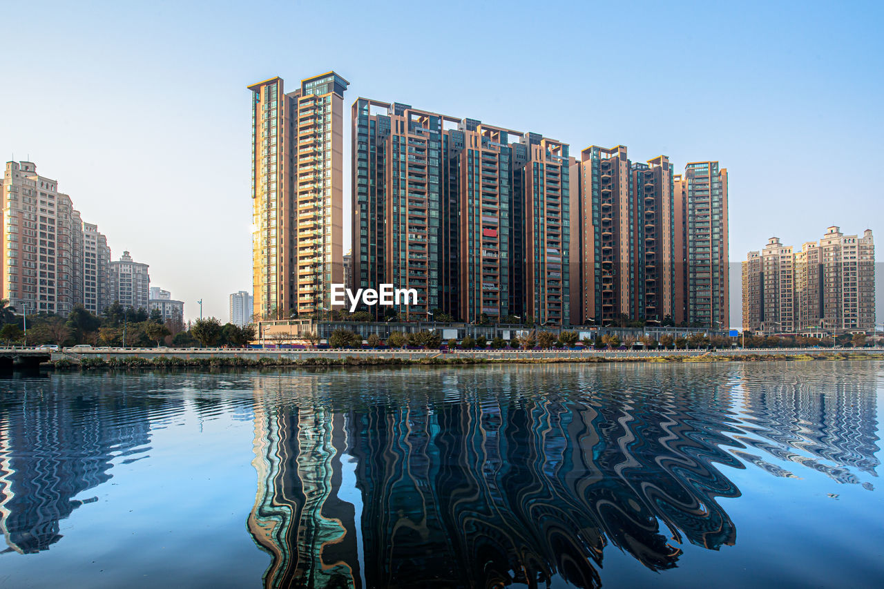 REFLECTION OF BUILDINGS IN WATER AGAINST CLEAR SKY