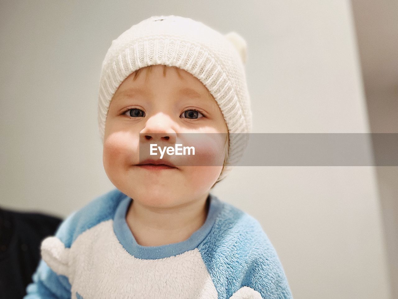 portrait, child, childhood, one person, skin, baby, cute, headshot, front view, innocence, hat, clothing, cap, looking at camera, indoors, toddler, knit cap, emotion, knit hat, portrait photography, person, baby clothing, white, close-up, human face, happiness, lifestyles, smiling, blue, casual clothing, looking, men, human head, babyhood