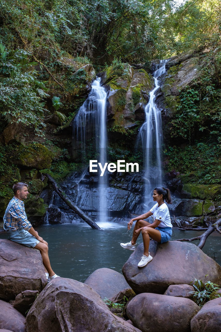 rear view of woman standing against waterfall in forest