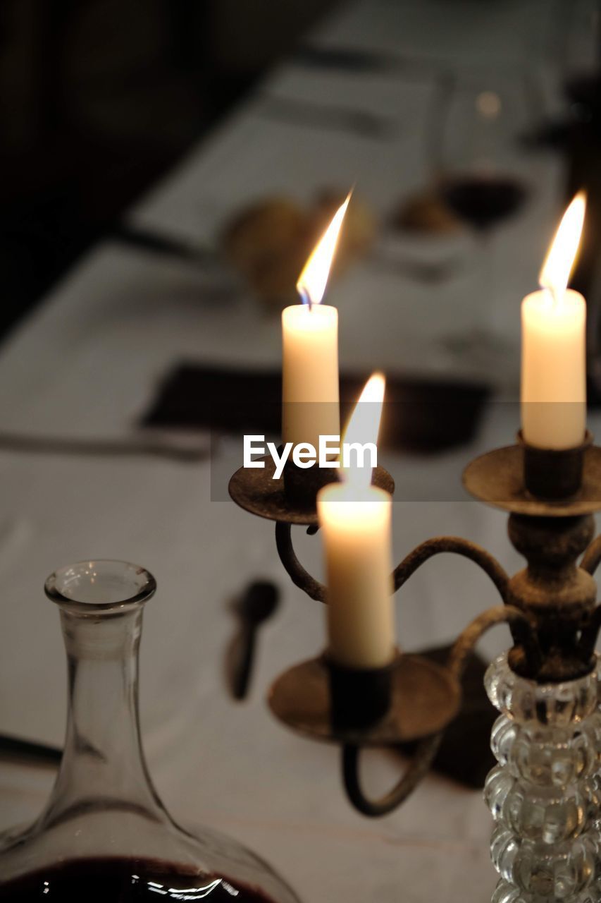 CLOSE-UP OF BURNING CANDLES ON TABLE