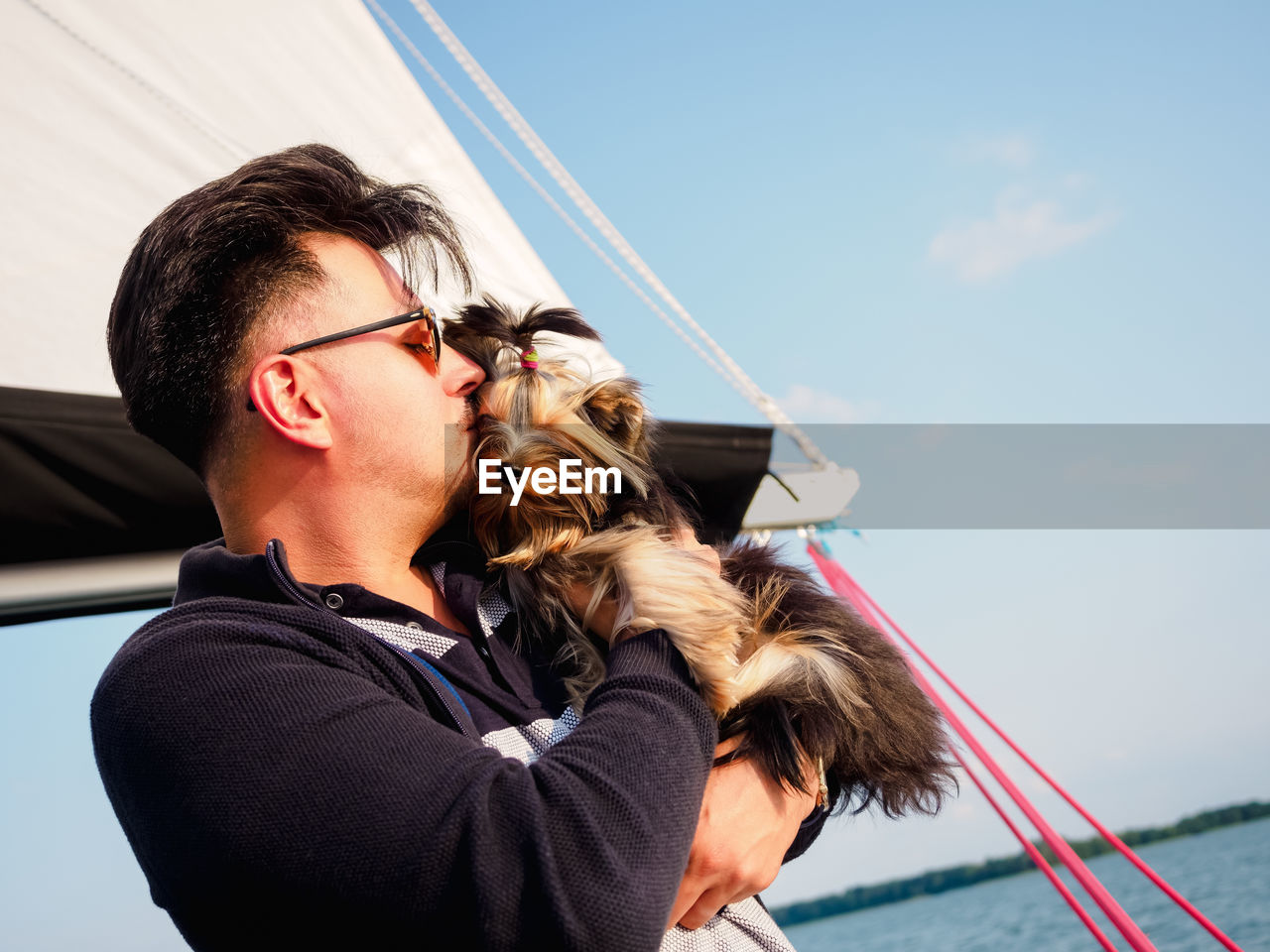 Handsome person hugs his small dog yorkshire terrier on a sailing yacht, travel with pets