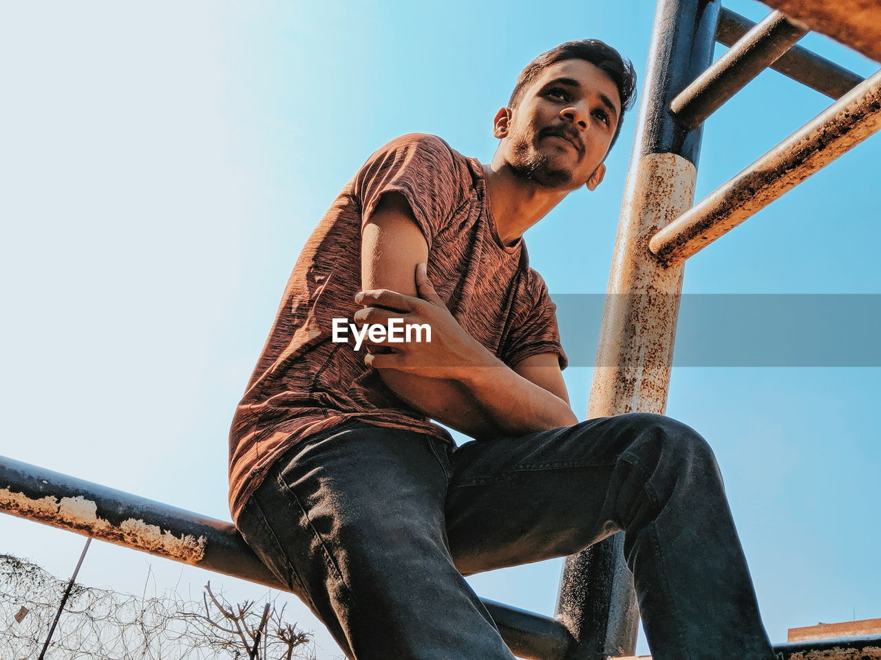 Low angle view of young man sitting against clear sky