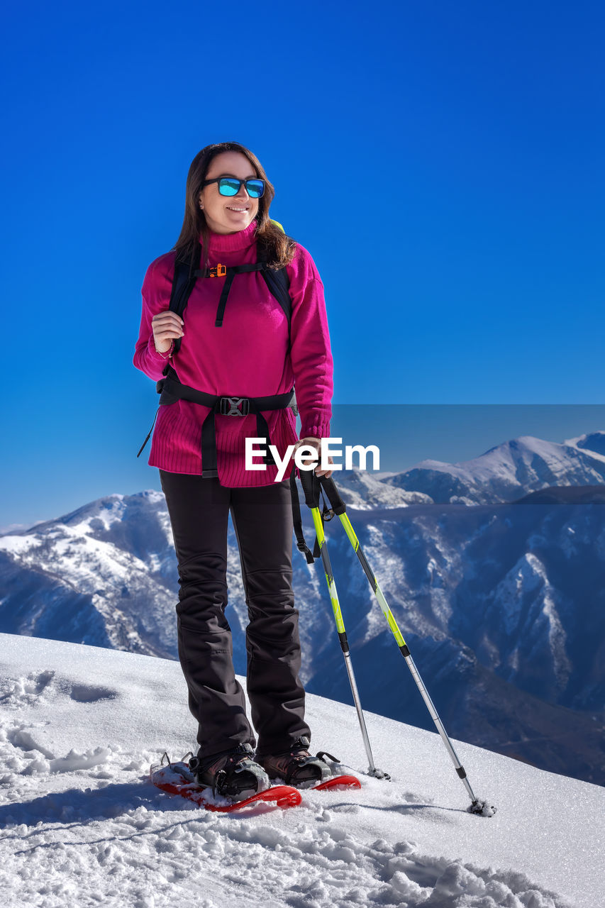 Snow hiker in the mountains, with snowshoes, snow poles and backpack. middle-aged woman, full length