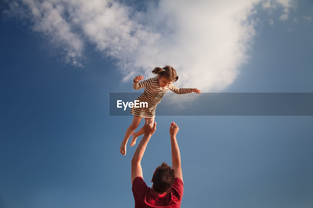 Low angle view of father tossing daughter mid air against sky
