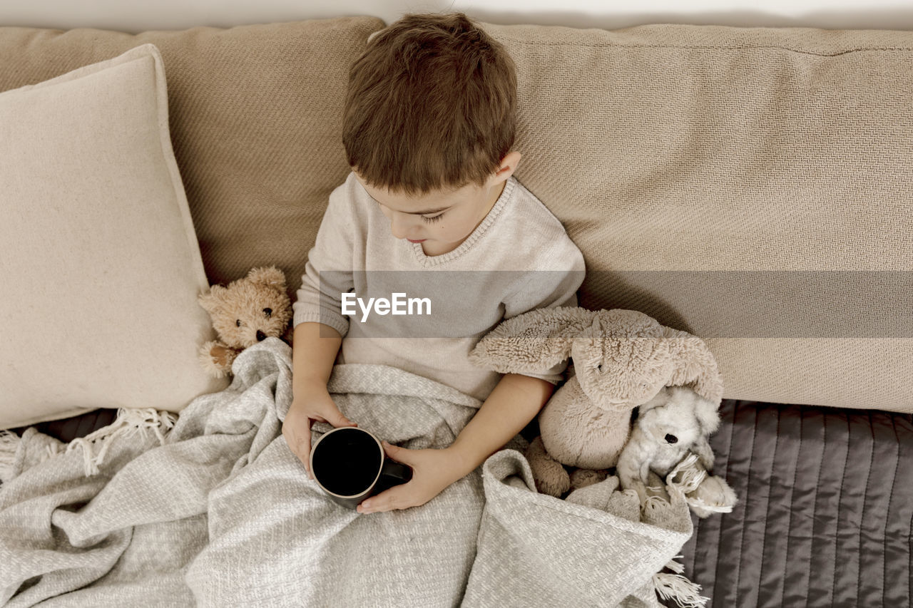 Sick little boy drinking hot tea on the bed at home. unwell, illness child wrapped in a blanket, 