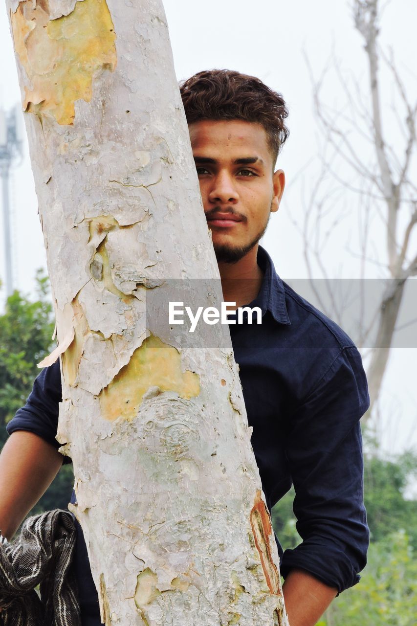 Full length of young man standing by tree trunk