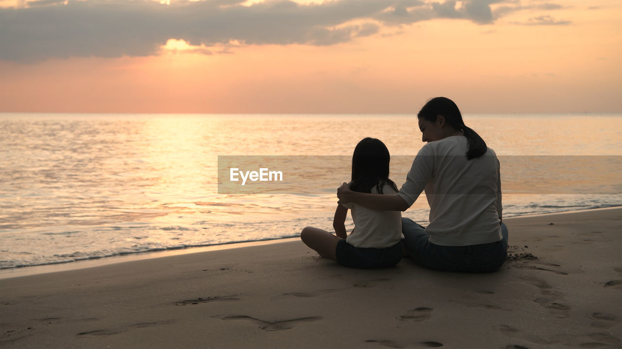 Rear view of women sitting on shore at sunset