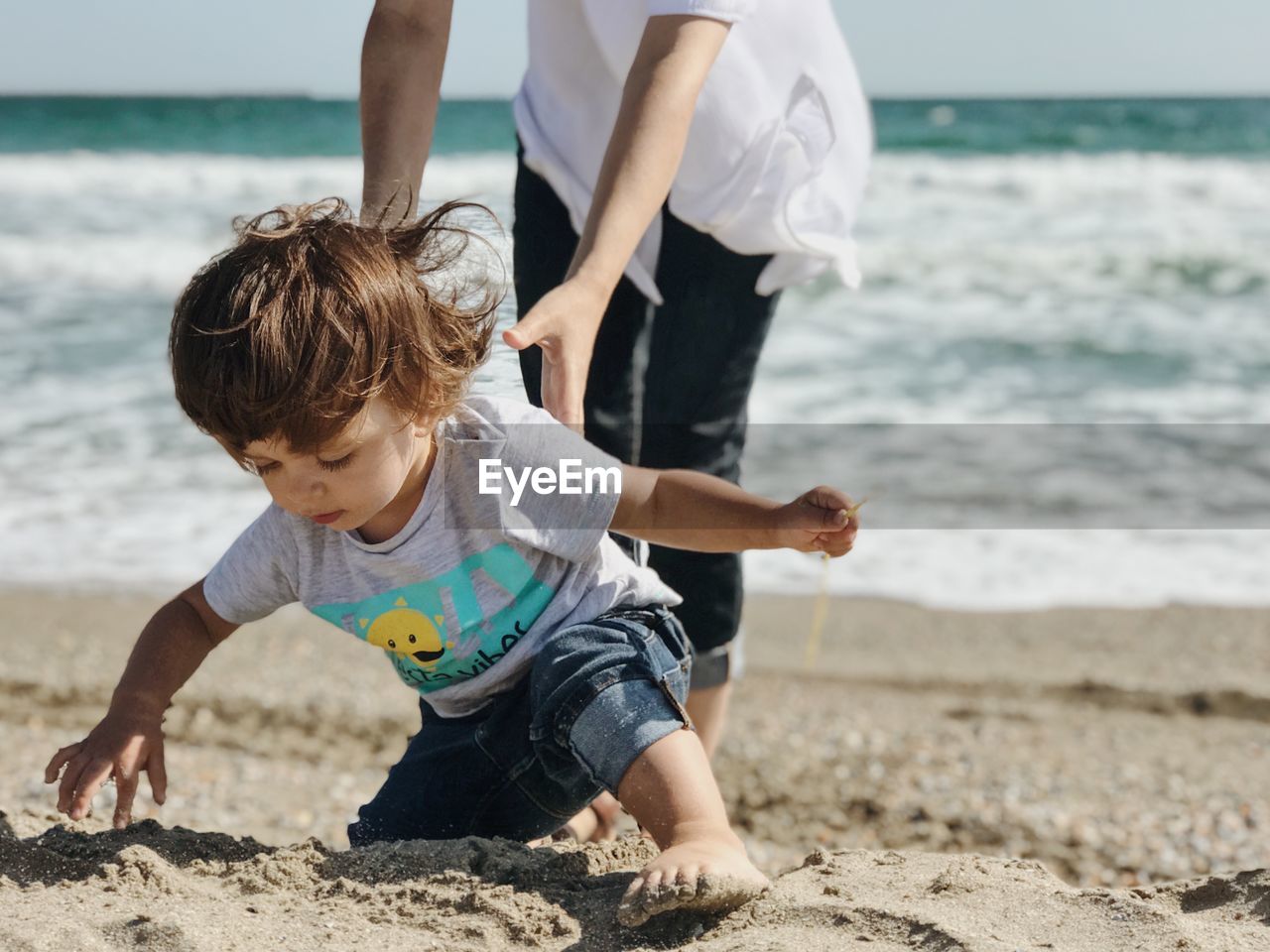 Low section of woman holding boy playing on sand at beach