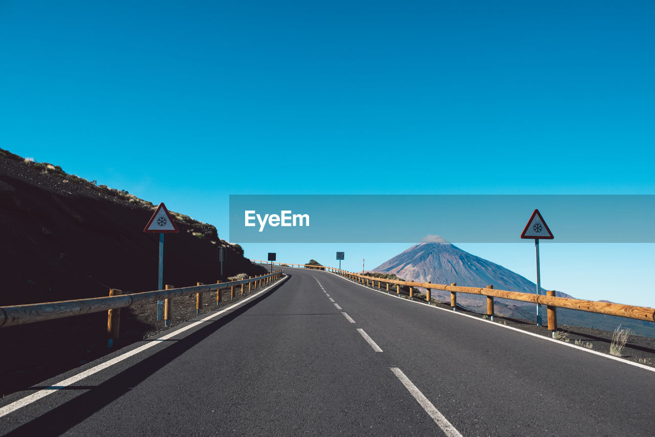 Road leading towards mountain against clear blue sky