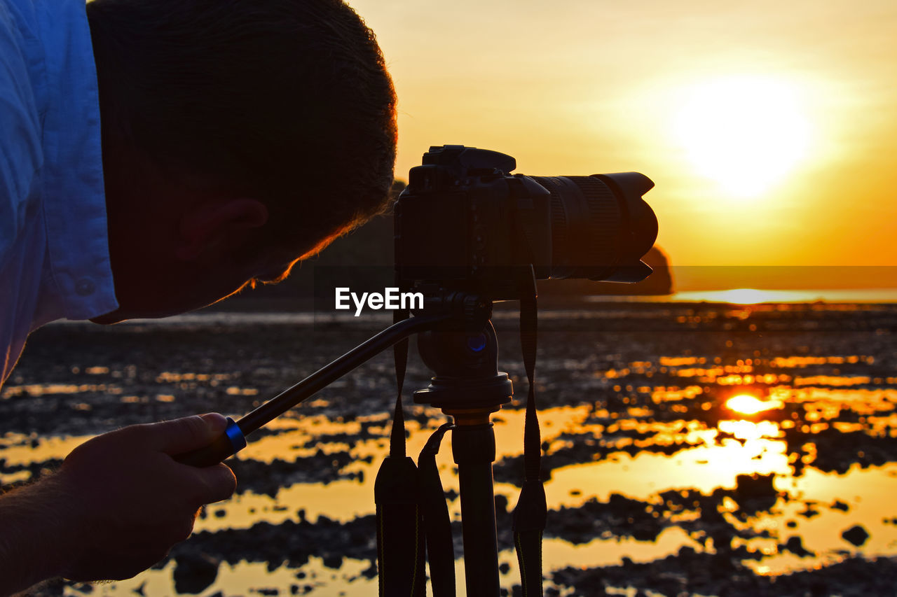 Photographer photographing at beach against sky during sunset