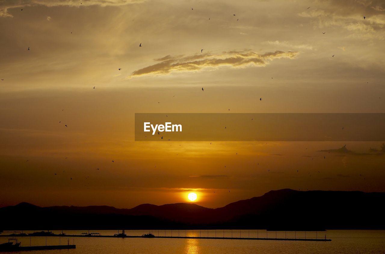 Scenic view of lake with jetty and boats by mountains at dusk