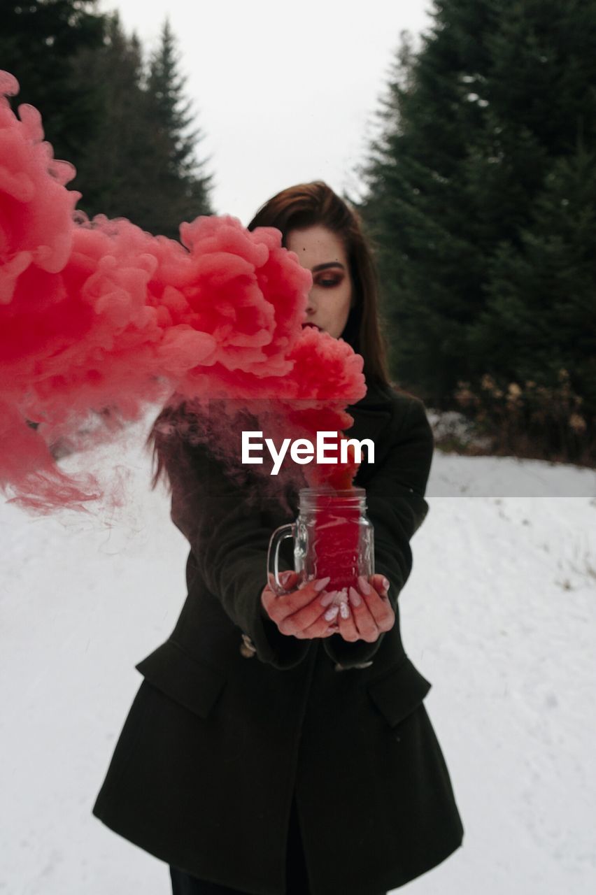 Woman holding red distress flare while standing on snow covered field