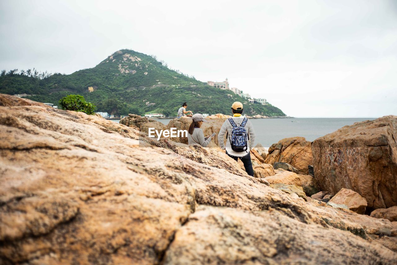 REAR VIEW OF PEOPLE WALKING ON ROCK AGAINST SKY