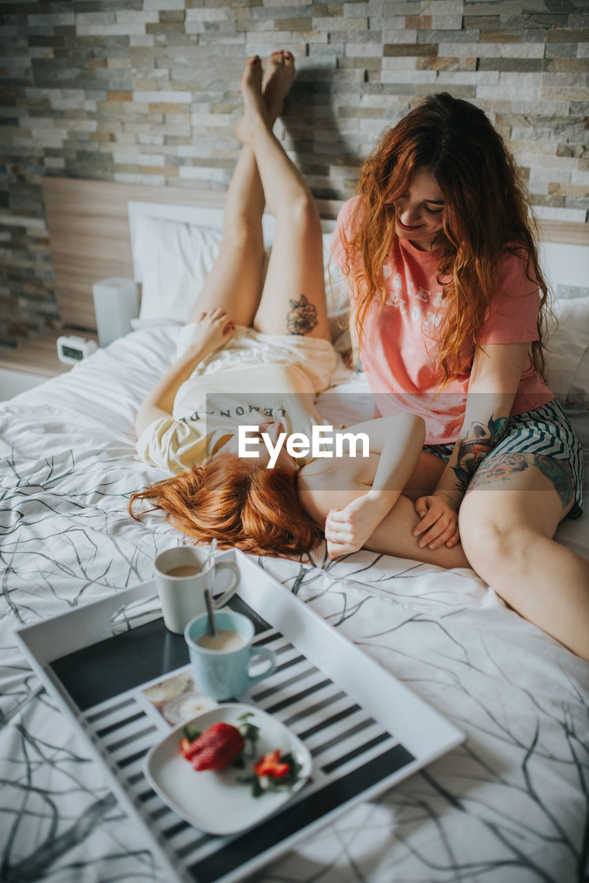 Young cheerful alternative couple in pajamas resting on bed near breakfast on tray in bedroom