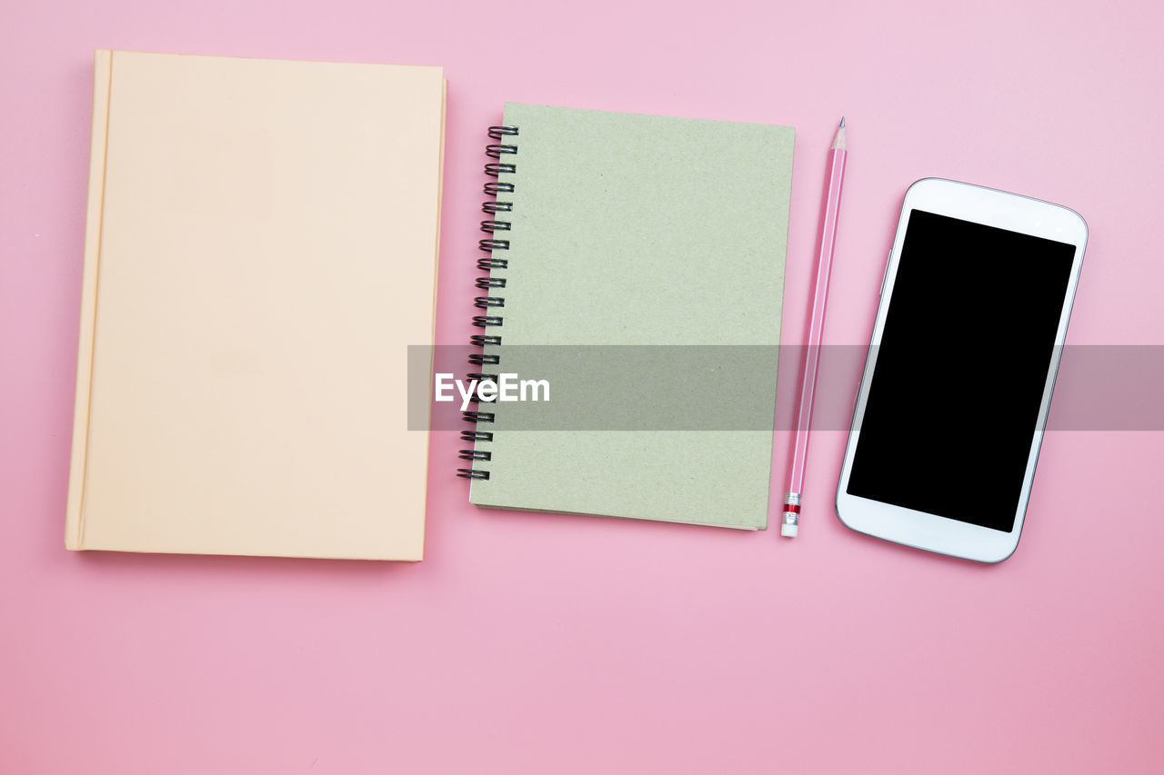 High angle view of smart phone with books and pencil over pink background