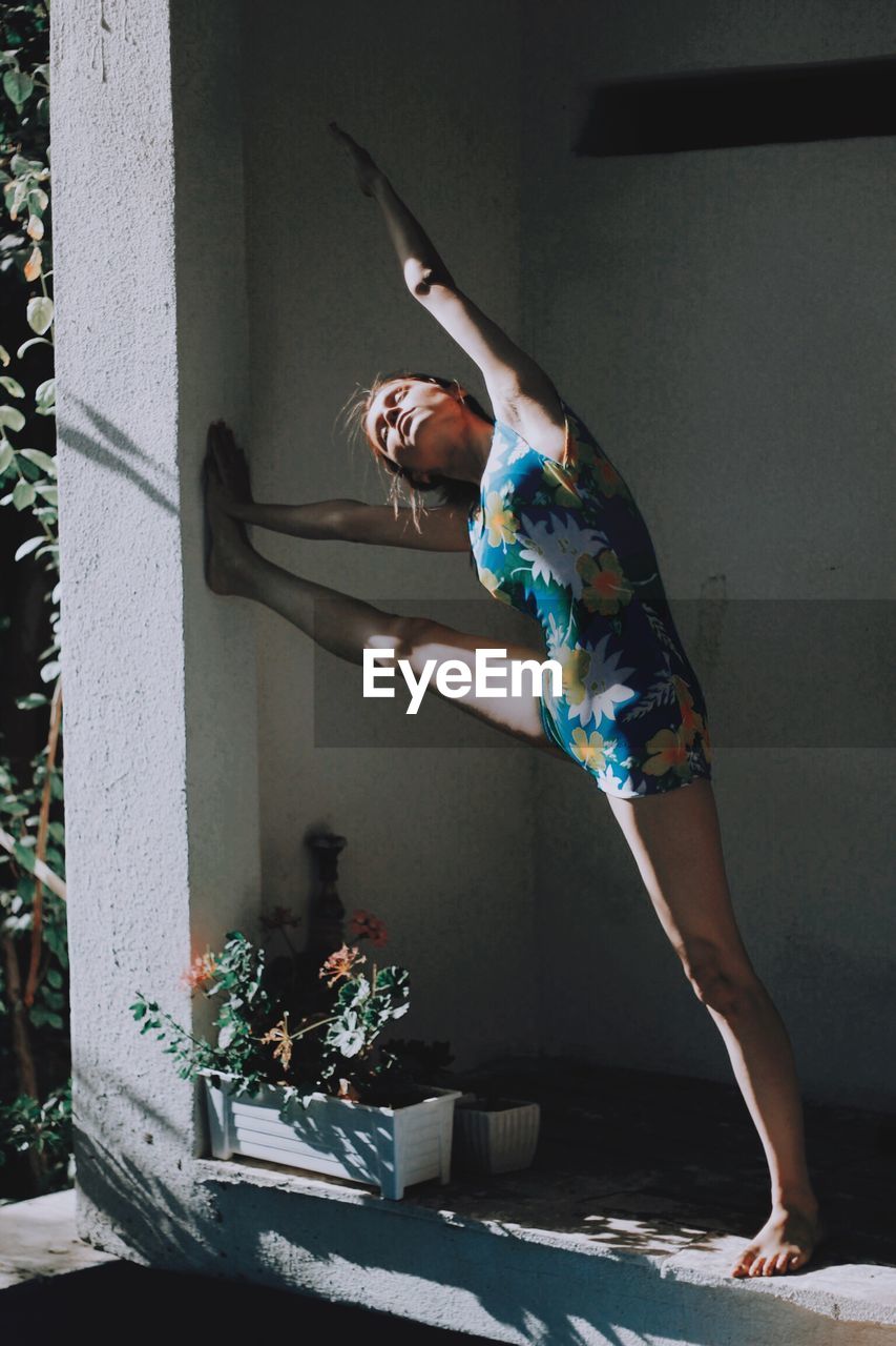 Full length of young woman exercising while standing by wall