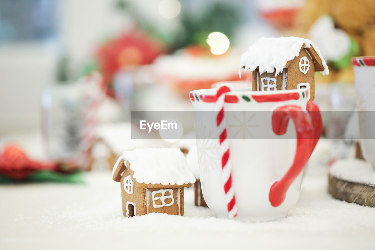 Close-up of gingerbread house and white mugs decorated on table during christmas