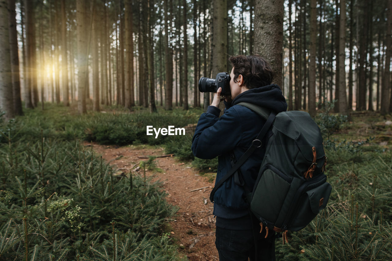 Rear view of man photographing in forest