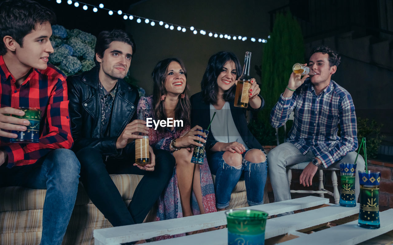Friends having drinks while sitting at patio during night