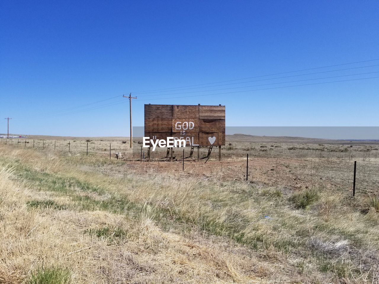 sky, landscape, natural environment, prairie, land, blue, clear sky, nature, grass, abandoned, no people, plain, environment, scenics - nature, day, non-urban scene, horizon, architecture, copy space, rural scene, field, built structure, remote, desert, ranch, plant, horizon over land, tranquility, rural area, sunny, outdoors, tranquil scene, wood, rundown, steppe, dry, power generation, sunlight, absence, fence, arid climate, hut, old