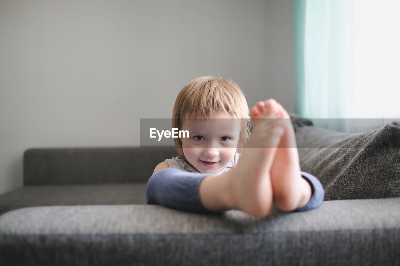 Child jumps and plays on sofa in minimalist living room, gray sofa.