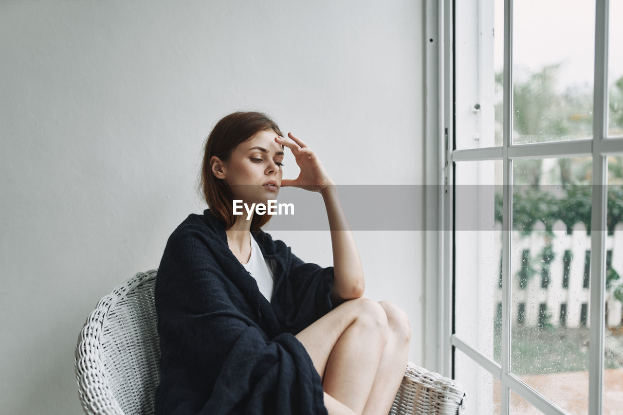 SIDE VIEW OF WOMAN SITTING IN WINDOW