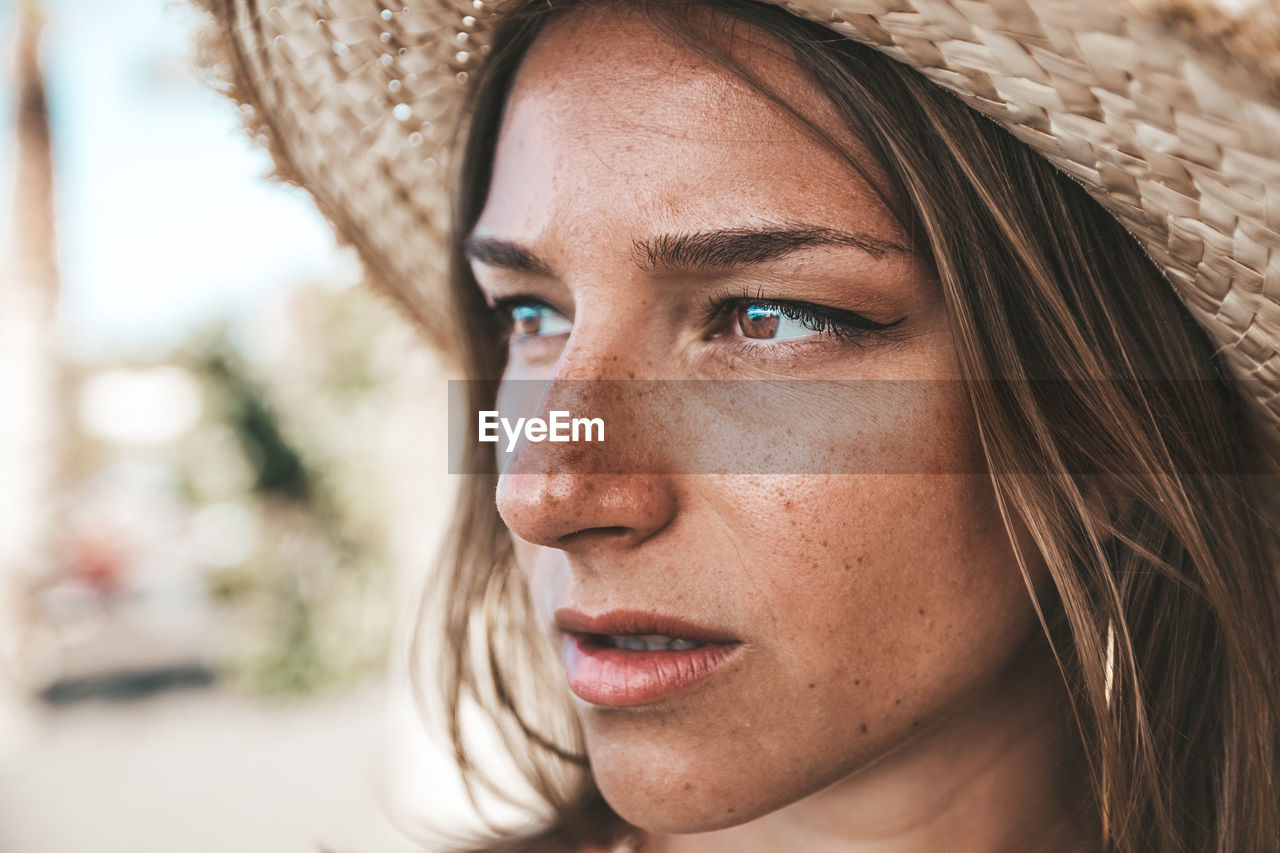 Close-up of young woman wearing hat looking away