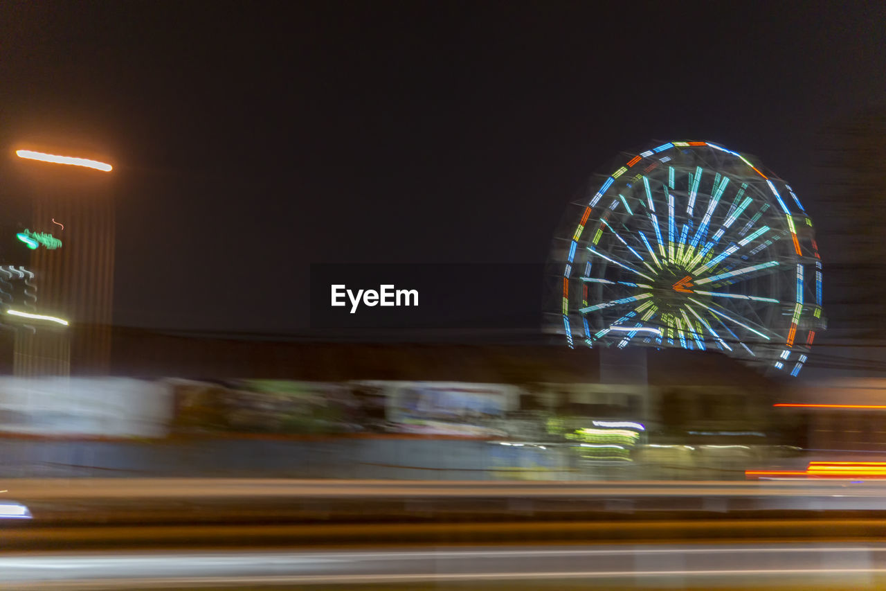 BLURRED MOTION OF ILLUMINATED FERRIS WHEEL AT NIGHT