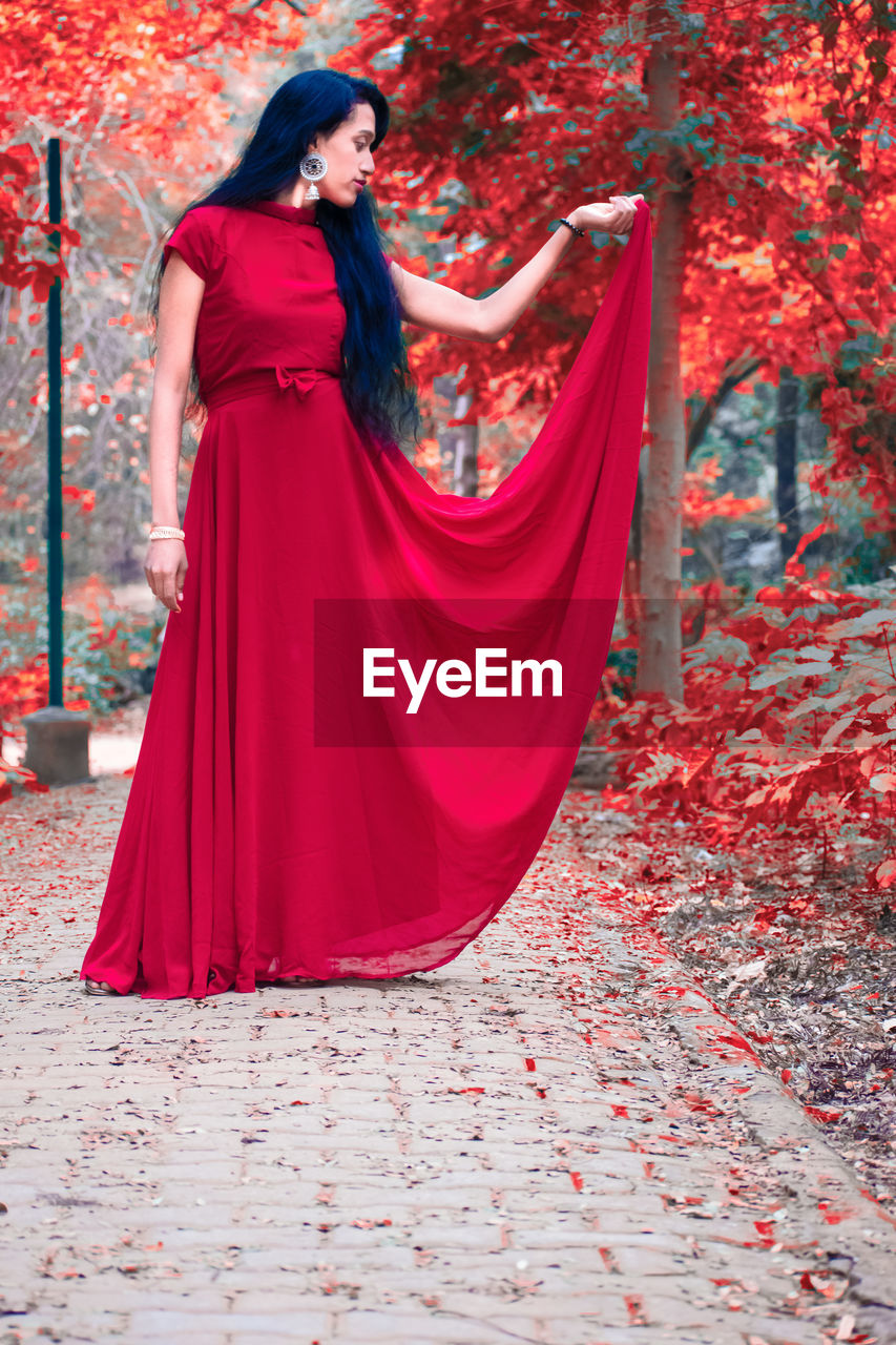 red, fashion, one person, clothing, adult, women, young adult, dress, full length, autumn, elegance, gown, glamour, portrait, hairstyle, leaf, nature, plant part, long hair, standing, tree, pink, outdoors, evening gown, arts culture and entertainment, spring, plant, looking, formal wear, female, brown hair, lifestyles, beauty in nature, looking at camera, photo shoot, smiling, day