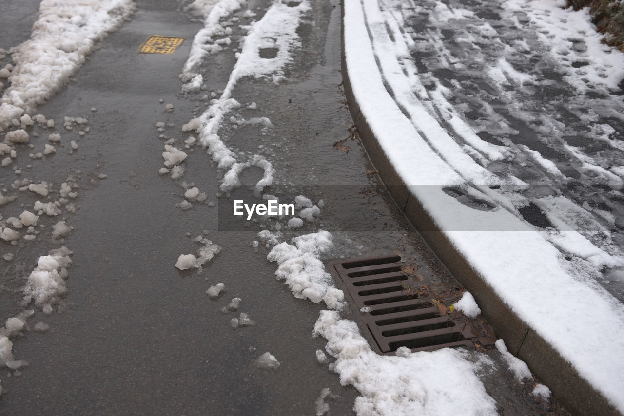 Road and pavement covered in thawing snow. road is partially cleared by cars