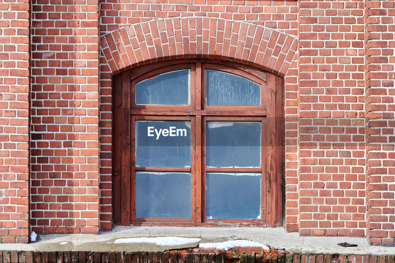 One arched glass window on old red brick wall. window in brown wooden frame on brick wall