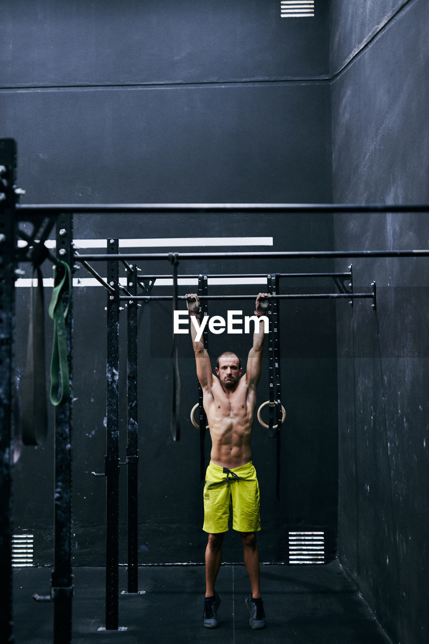 Shirtless fit young man working out in a cage at indoors gym