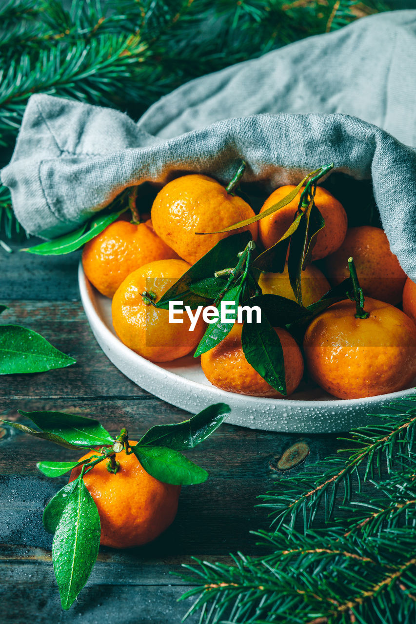 Tangerines with green leaves on a green wooden table in a rustic style surrounded by spruce branches