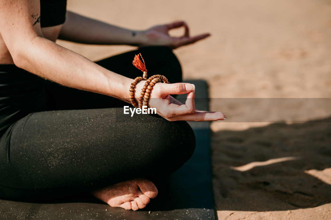 Cropped side view of unrecognizable female in sportswear sitting on mat in padmasana with mudra hands and meditating while practicing yoga with closed eyes on beach