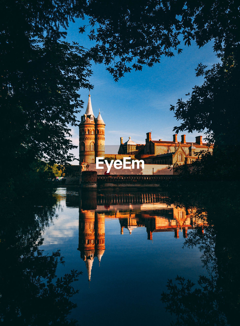 Reflection of buildings in lake amidst trees against sky