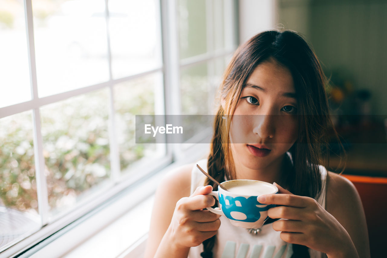 Portrait of young woman drinking coffee cup while sitting at home