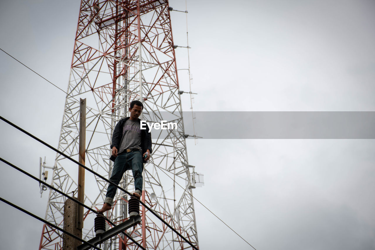 LOW ANGLE VIEW OF MAN WORKING AGAINST THE SKY