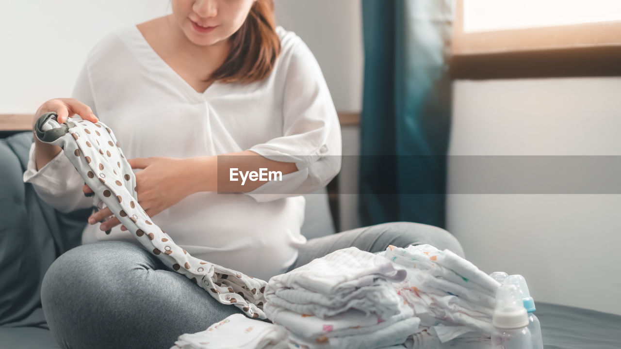 Midsection of woman holding white while sitting at home