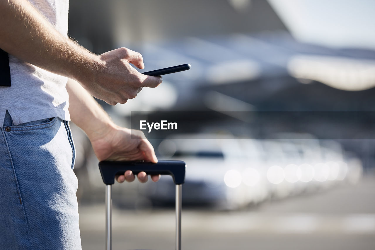 Man holding smartphone and using mobile app against a row of taxi cars.