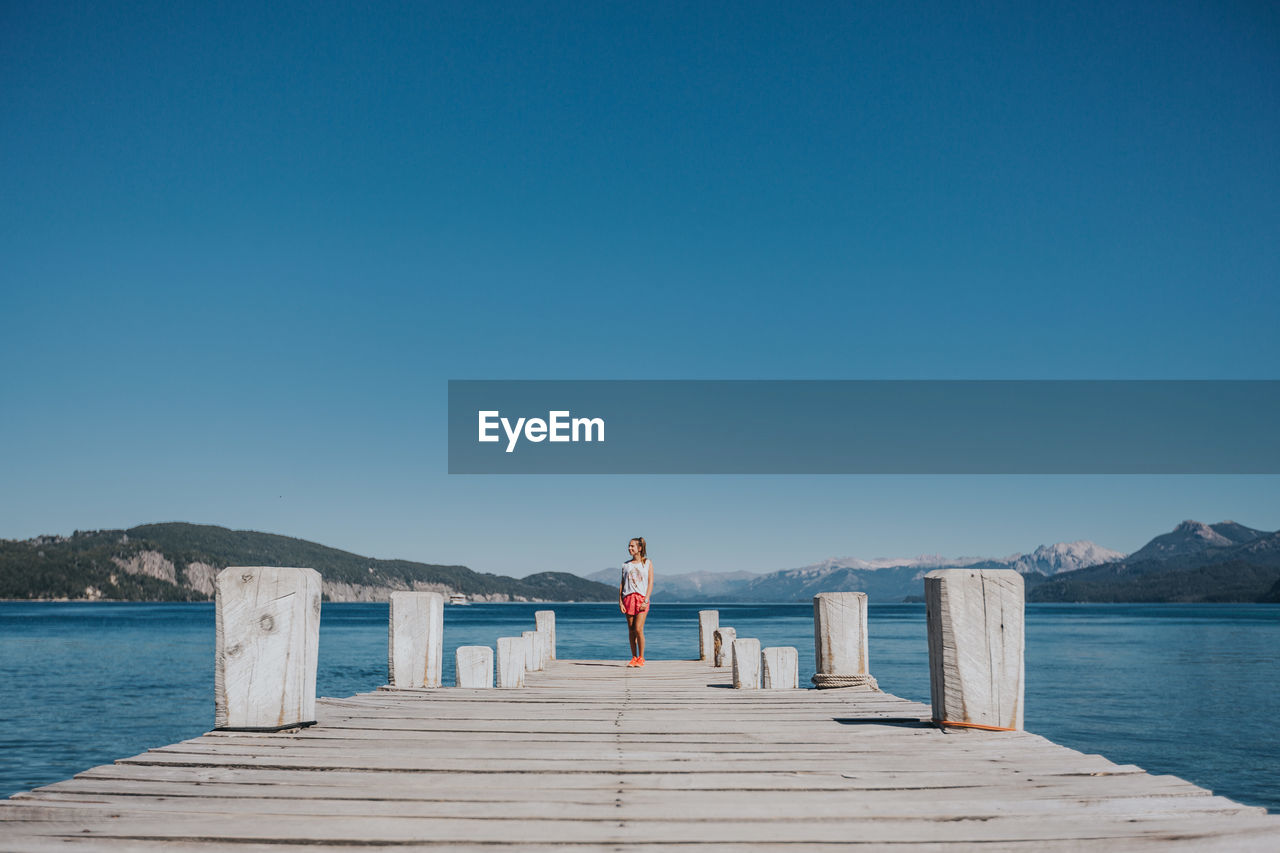 View of woman standing on pier against clear blue sky