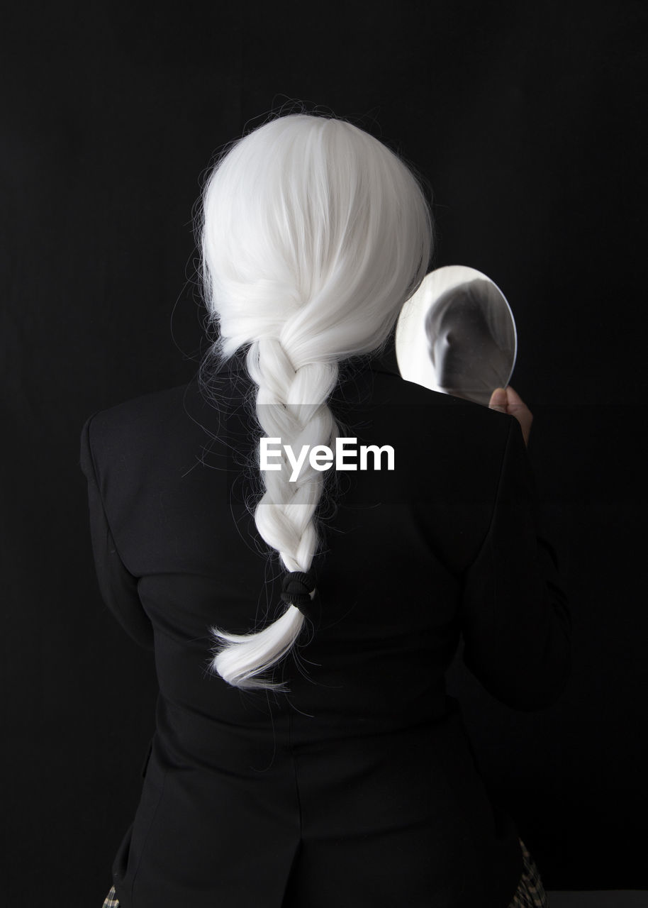 Rear view of woman holding mirror while standing against black background