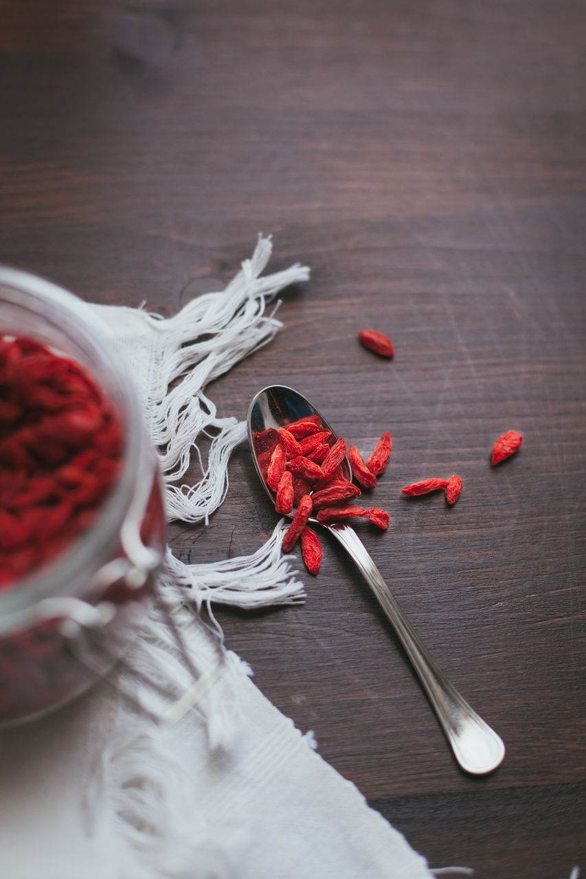 Directly above shot of red dried food in spoon on wooden table