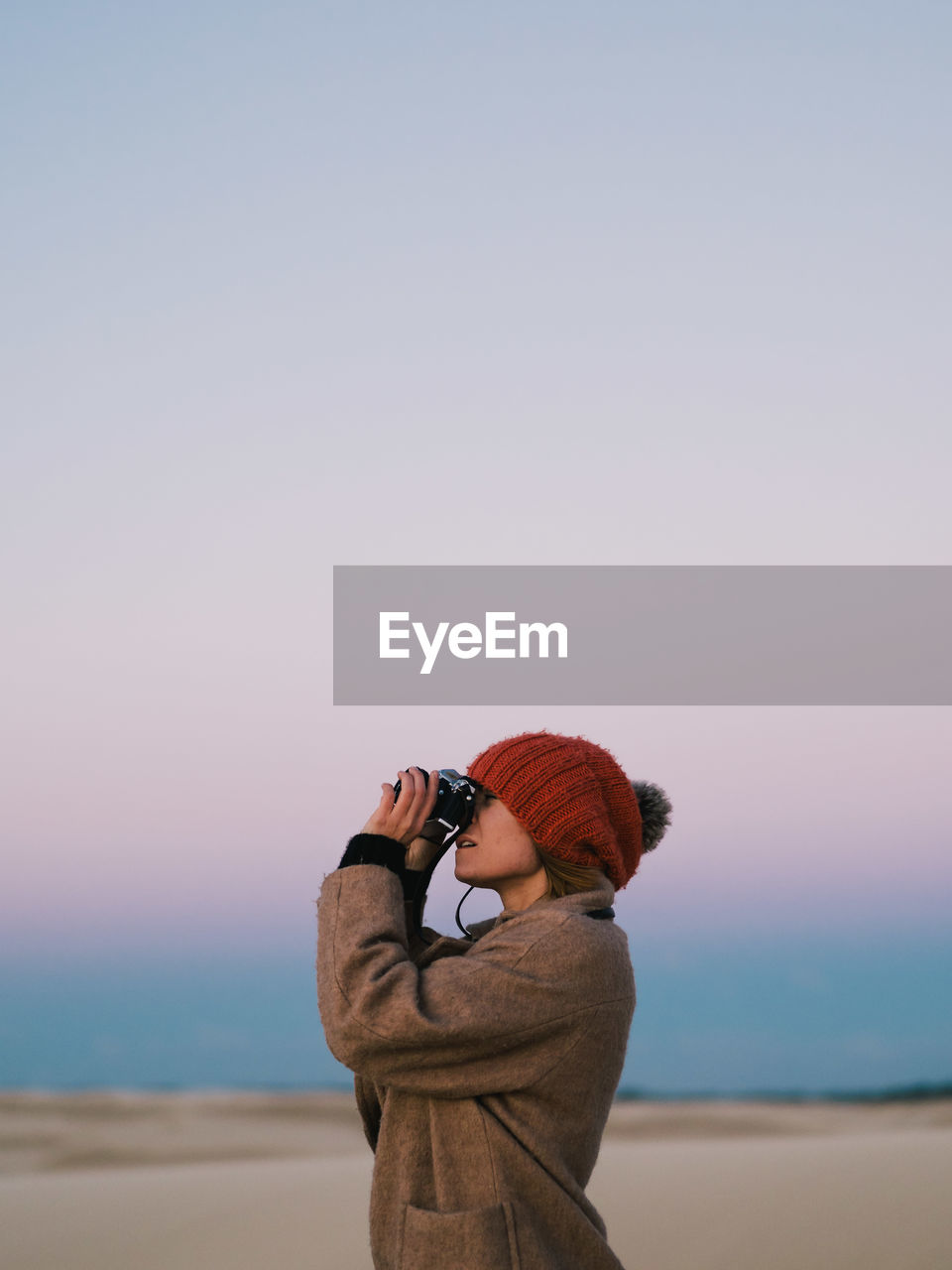 Side view of man looking through binoculars while standing against sky