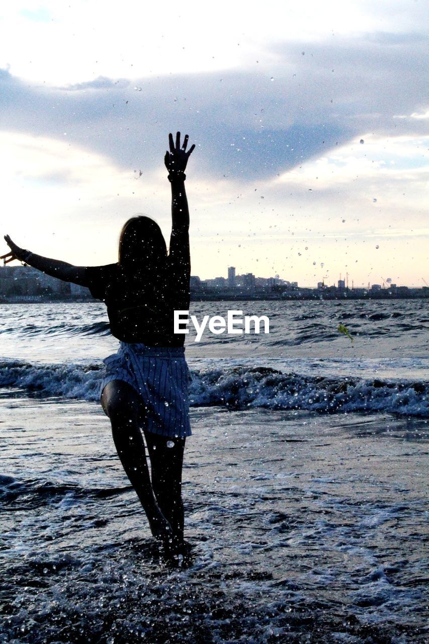 Rear view of woman dancing on beach against sky